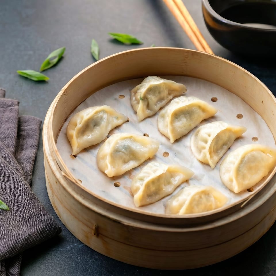 Steamed dumplings in a bamboo steamer with chopsticks, a black bowl, and chili oil.