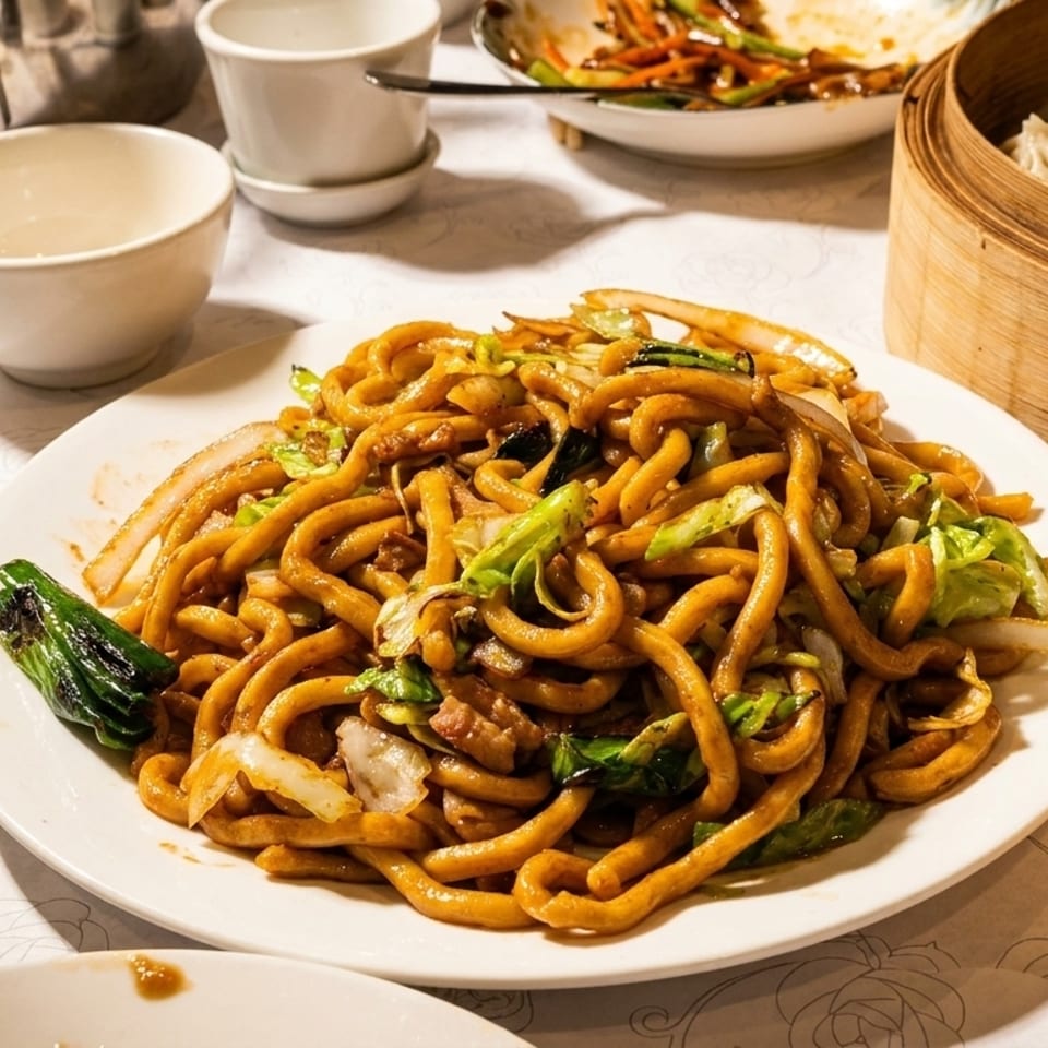A plate of stir-fried noodles with cabbage and onions, alongside dim sum and tea cups.